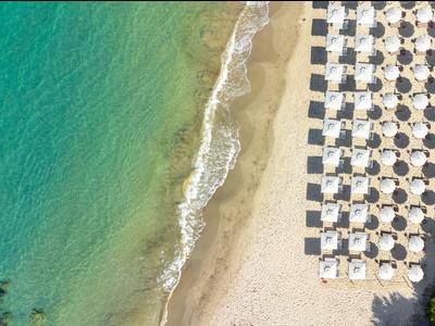Letecký pohled na pláž s řadami slunečníků a tyrkysovou vodou.