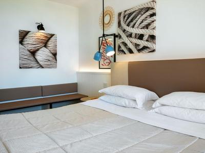 Moderní hotelový pokoj s manželskou postelí, uměním na stěně a závěsnou lampou vedle postele.