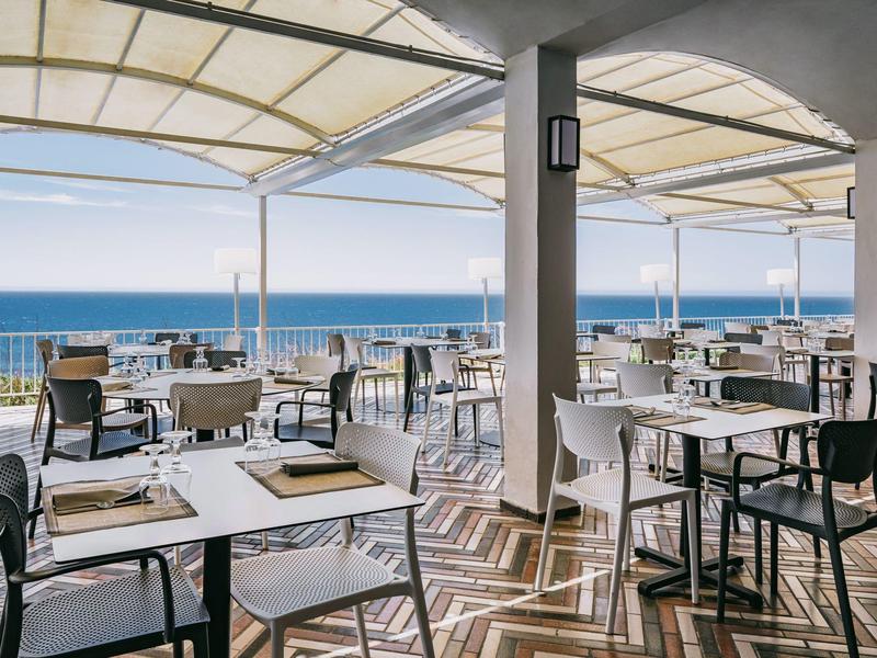 Terasa restaurace s výhledem na moře, prostřené stoly a moderní židle.