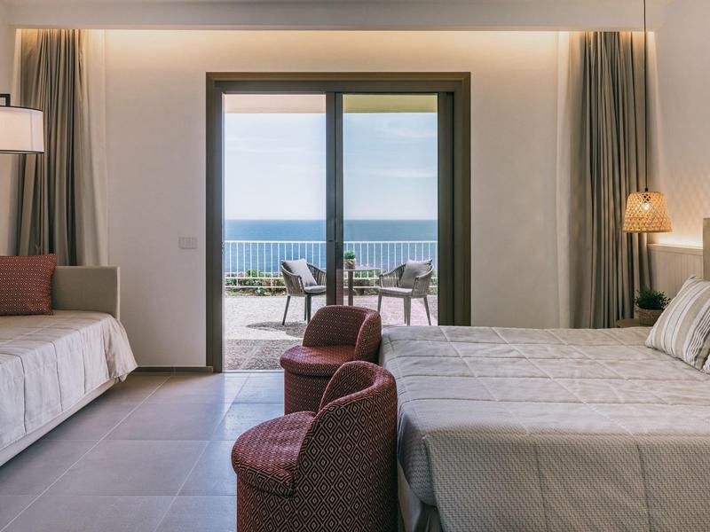 Moderní hotelový pokoj s manželskou postelí, posezením a balkonem s výhledem na moře.