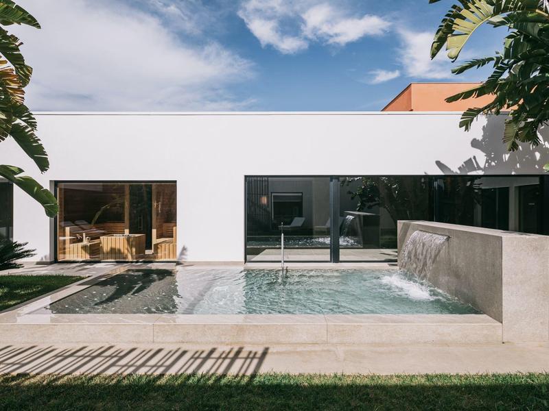 Moderní bazénová oblast s prostorným vířivým bazénem před bílou budovou a zeleným trávníkem.