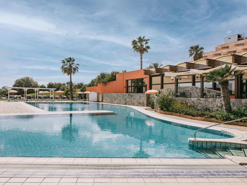 Moderní venkovní bazén s lehátky a palmami v slunném hotelovém resortu.