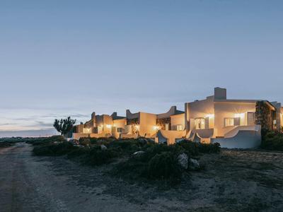 Rijhuizen op het strand bij schemering met verlichte ramen en een heldere hemel.