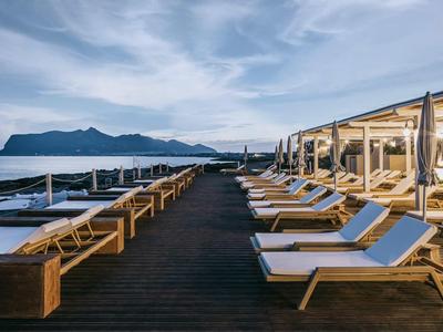 Strandstoelen op een houten terras met uitzicht op zee en bergen onder een heldere lucht.