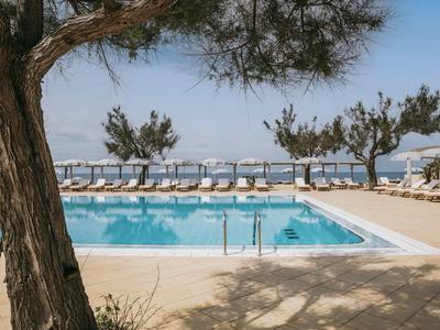 Helder zwembad omgeven door ligstoelen en bomen met uitzicht op de zee.