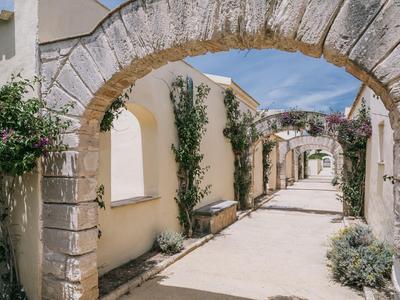 Slunná středomořská stezka se žlutými zdmi a kvetoucími rostlinami pod kamenným obloukem.