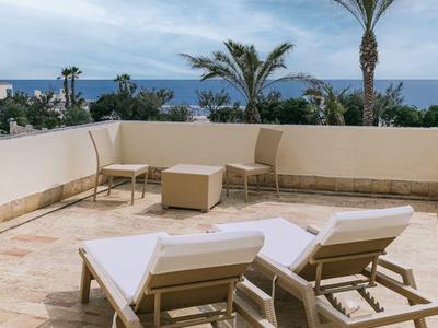 Terras met twee ligstoelen met uitzicht op zee en palmbomen onder een bewolkte lucht.