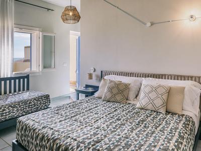 Pohodlný hotelový pokoj s manželskou postelí, křeslem a otevřeným oknem.