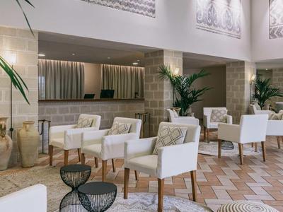 Lichte hotelkamer met witte stoelen, tapijten en planten in een modern interieur.