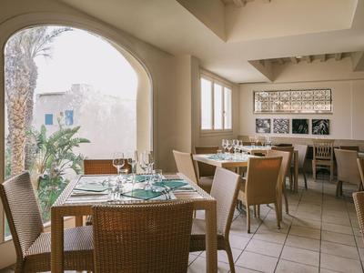 Světla restaurace s prostřenými stoly a výhledem na terasu s palmami.