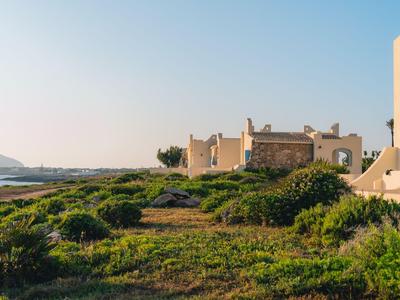 Hotel ve stylu resortu s výhledem na moře, obklopený zelenou vegetací pod jasnou oblohou.