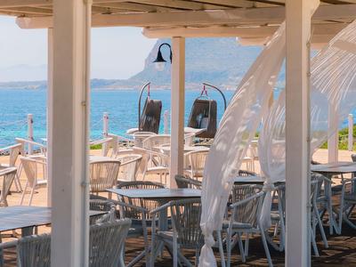 Otevřená restaurace s stolky a židlemi u moře s výhledem na hory.