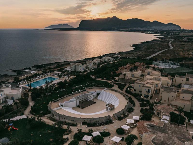Luchtfoto van een resort met zwembad en podium aan zee bij zonsondergang.