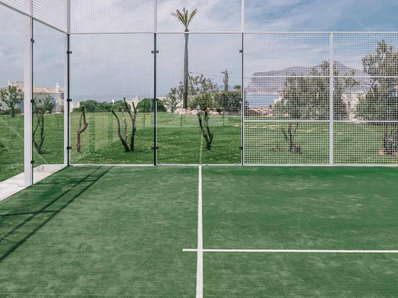 Groene tennisbaan met witte lijnen en hek onder bewolkte lucht