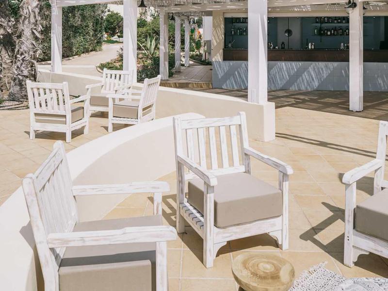 Terras met wit houten meubilair en pergola onder heldere hemel met palmbomen.