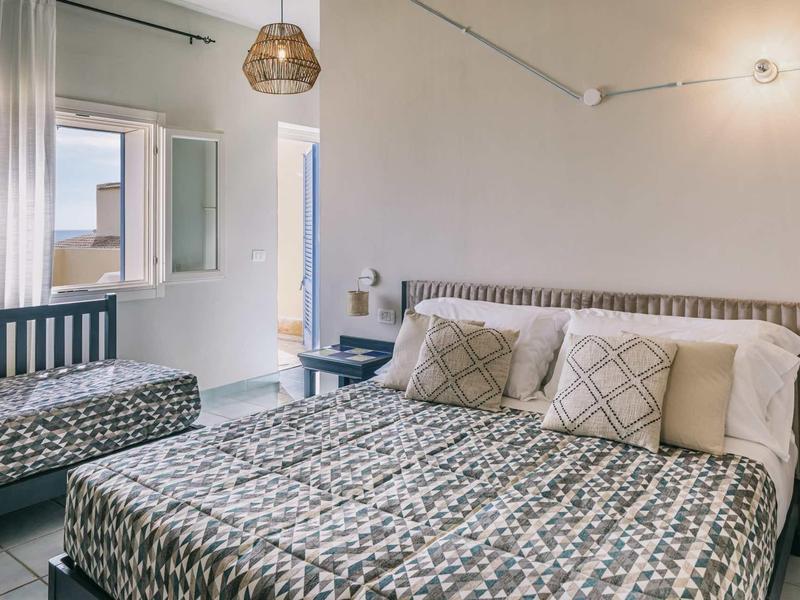 Knusse hotelkamer met tweepersoonsbed, bank, raam en neutraal kleurenpalet.