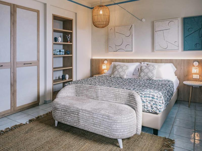 Gezellige hotelkamer met groot bed, bankje, tapijt en minimalistische inrichting.