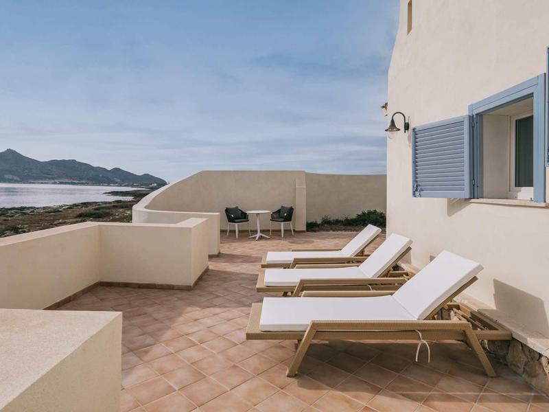 Terras met ligstoelen en stoelen met uitzicht op zee onder een blauwe lucht.