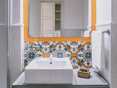 Moderní koupelna s velkým zrcadlem, bílým umyvadlem a dekorativními dlaždicemi.