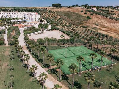 View of tennis courts next to a hotel surrounded by palm trees and fields.