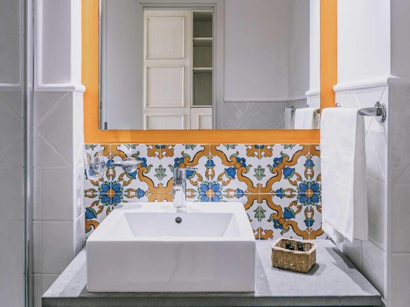 Moderní koupelna s velkým zrcadlem, bílým umyvadlem a dekorativními dlaždicemi.