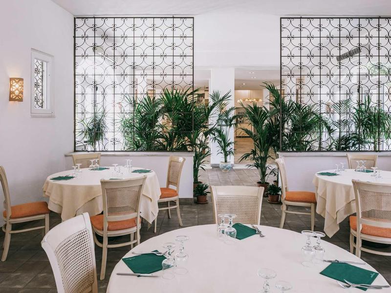 Elegantní restaurace s kulatými prostřenými stoly a velkými rostlinami jako příčkami.