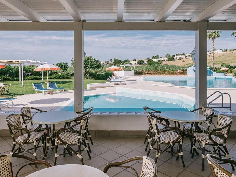 Bazén s lehátky a stoly pod zastřešenou oblastí v rekreačním středisku.