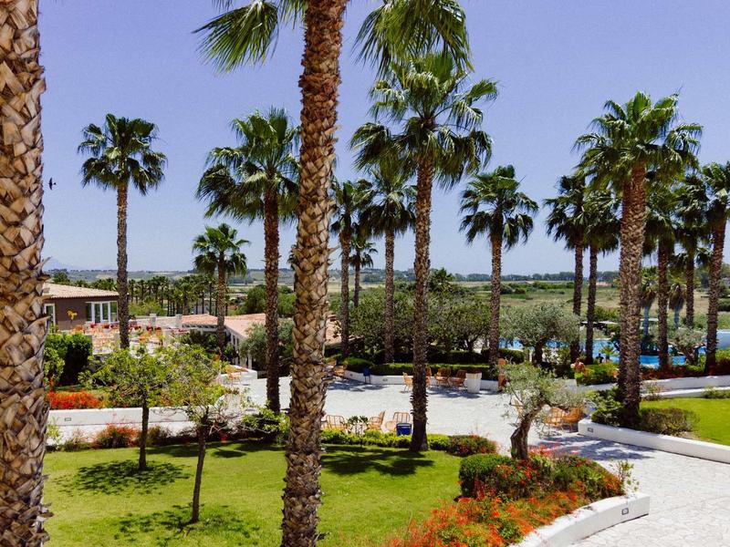 Zelená zahrada s palmami a chodníkem vedle velkého bazénu v hotelovém letovisku.