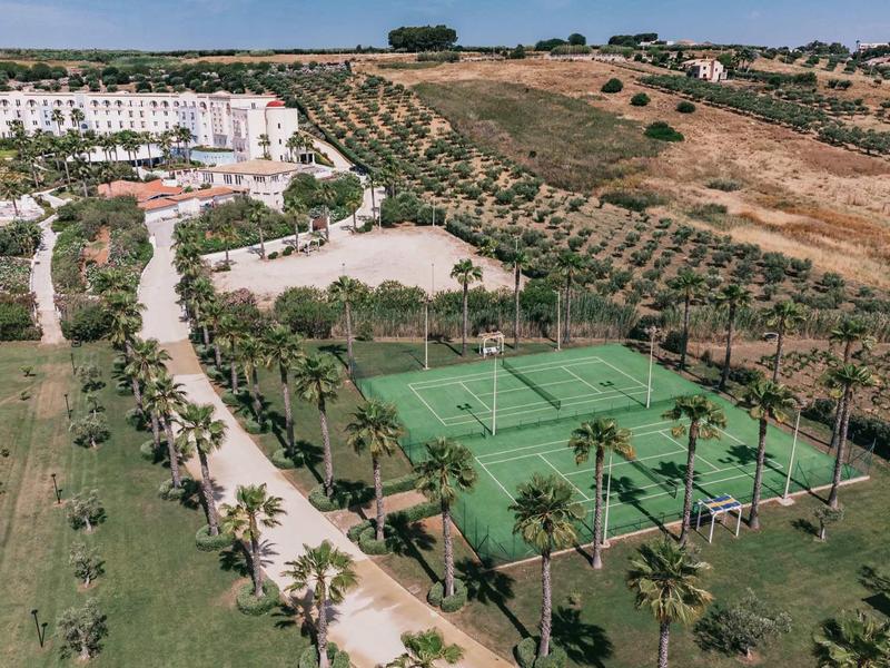 Hotelový komplex s tenisovými kurty obklopenými palmami a olivovým sadem.