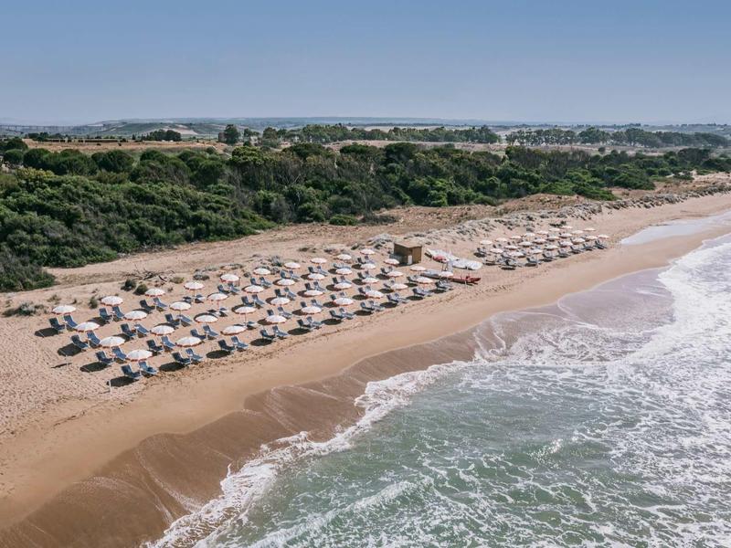 Rozlehlá písečná pláž s slunečníky a výhledem na zelené duny a modrou oblohu.