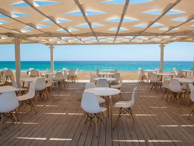 Open seating area with chairs and tables overlooking the sea under a patterned sunshade.