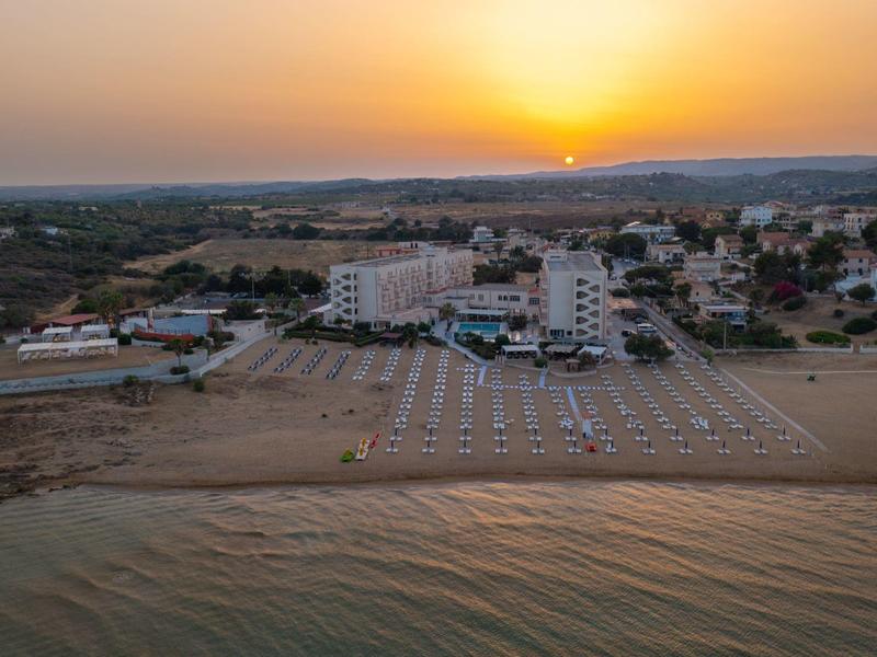 Beach hotel at sunset with calm water and sandy shore.