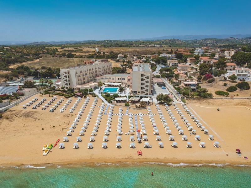 Large hotel with pool on sandy beach and many loungers by the sea.
