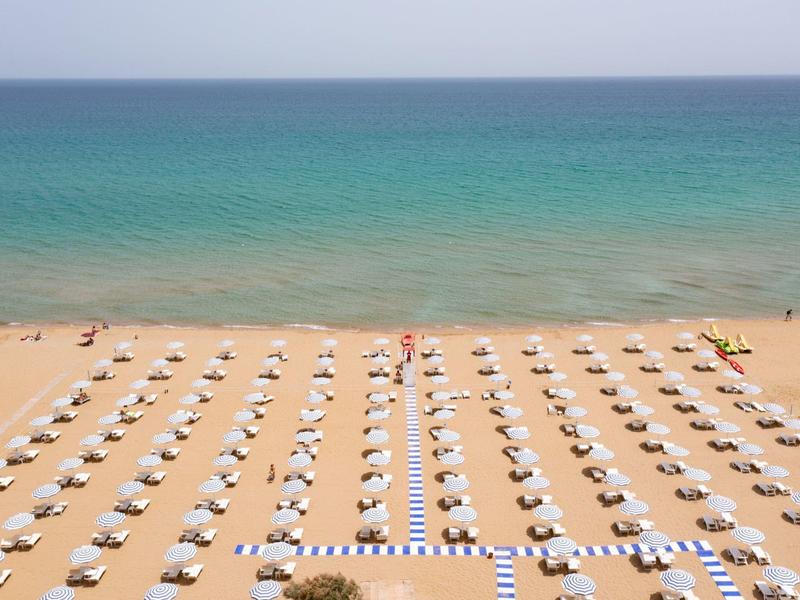 Beach with white sun umbrellas and loungers by calm blue-green sea.