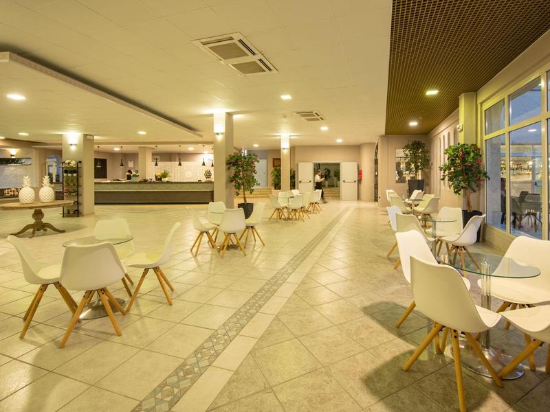 Spacious modern hotel lounge area with white chairs and tables, brightly lit.