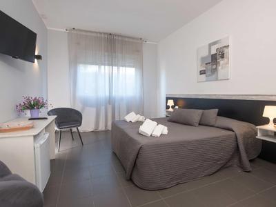 Nowoczesny pokój hotelowy z podwójnym łóżkiem, stolikami nocnymi, telewizorem i oknem z zasłoną.