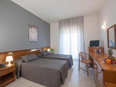 Nowoczesny pokój hotelowy z dwoma łóżkami pojedynczymi, biurkiem i oknem z jasnymi zasłonami.