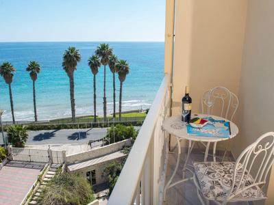 Balkon mit Tisch, Stühlen, Weinflasche und Meerblick mit Palmen.