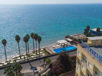 Blick auf ein Hotel mit Pool und Palmen am Meer bei sonnigem Wetter.