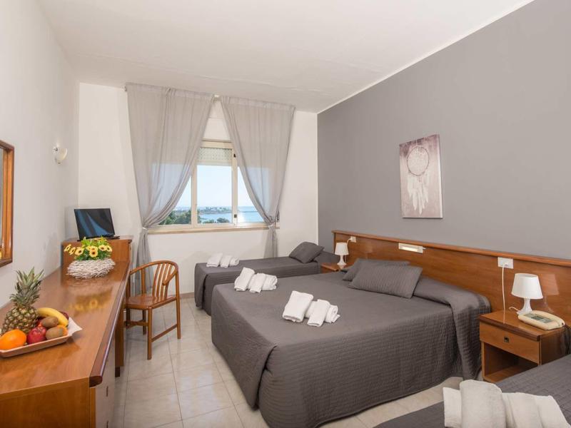 Pokój hotelowy z dwoma łóżkami, szarymi narzutami, drewnianymi meblami i oknem z widokiem na zewnątrz.