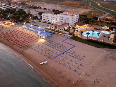 Hotel mit beleuchtetem Pool und Sonnenschirmen am Strand bei Dämmerung.