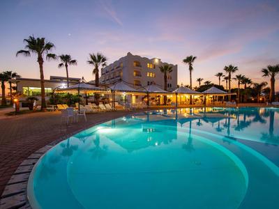 Hotel mit beleuchtetem Pool und Palmen bei Sonnenuntergang.