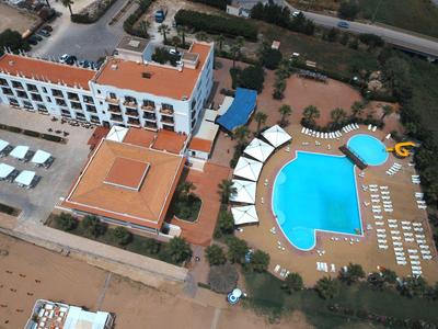 Vue aérienne d'un hôtel avec piscine, chaises longues et zone de plage adjacente.