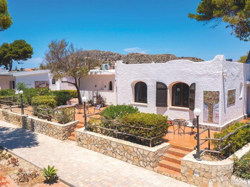 Weißes Gebäude mit Bogenfenstern in sonniger, mediterraner Umgebung.