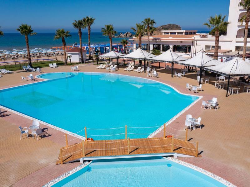 Großer Außenpool mit Sonnenschirmen und Blick auf das Meer und Palmen.