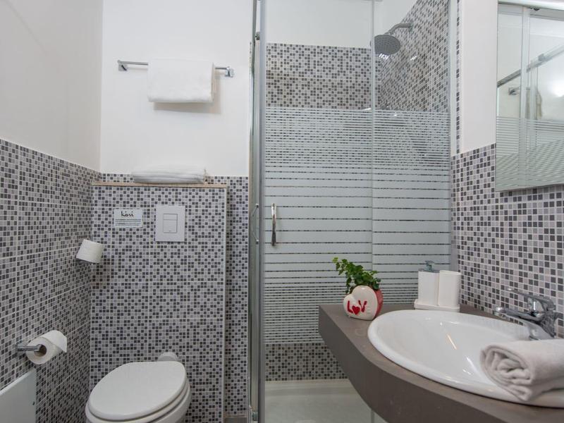 Kleines Badezimmer mit Dusche, weißer Toilette, Waschbecken und grauen Mosaikwänden.