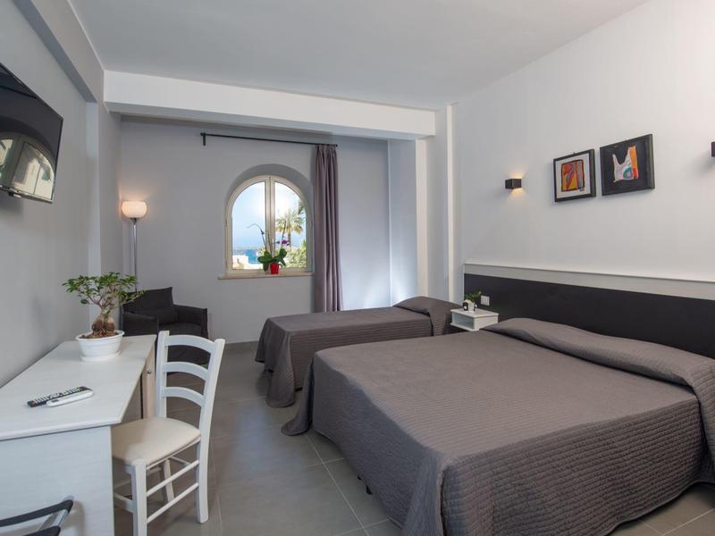 Modernes Hotelzimmer mit zwei Betten, Schreibtisch, Stuhl, Fernseher und dekorativen Bildern an der Wand.