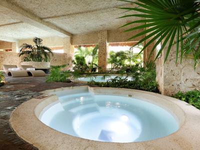 Moderner Whirlpool in einer tropischen Hotelhalle mit Grünpflanzen und Liegestühlen.