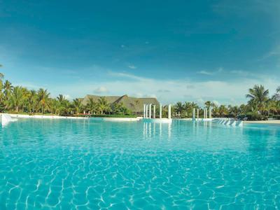 Klare blaue Lagune mit Pavillons und tropischer Vegetation im Hintergrund.