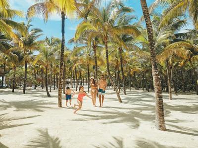 Familie mit kleinen Kindern läuft im tropischen Palmenwald auf hellem Sandstrand.